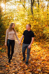 Young couple is having a walk in the sunny autumn park, forest. Happy man and his woman are hugging . Fallen yellow leaves, brith warm autumn weather. Autumn love story in park
