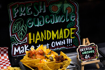 plate of nachos fries with beans and assorted vegetables garnished with melted cheese sauce with a very striking and colorful beautiful chalkboard sign