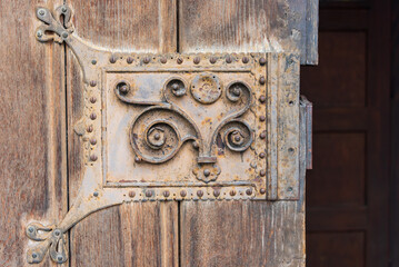 Close-up of an old wooden decorated door with carved wood with corroded and rusty fittings, elements of a decorative metal lock, door handle - 484991034