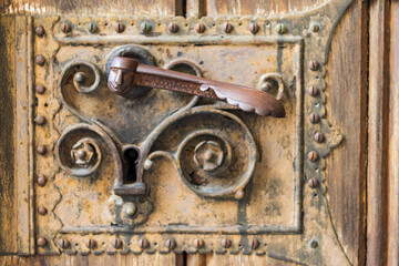 Close-up of an old wooden decorated door with carved wood with corroded and rusty fittings, elements of a decorative metal lock, door handle - 484991063