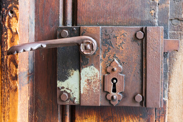 Close-up of an old wooden decorated door with carved wood with corroded and rusty fittings, elements of a decorative metal lock, door handle - 484991068