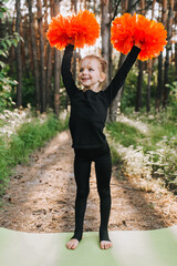 A beautiful, smiling girl athlete professional, a child cheerleader in a black suit stands on a...