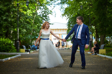 Young beautiful couple walk in nature in summer day. The bride in white dress with a long veil and...