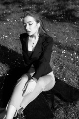 Black and white portrait of a young girl in the city park. Elegant and melancholy portrait, the girl is sitting on the grass. Beautiful woman in classic clothes