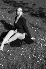 Black and white portrait of a young girl in the city park. Elegant and melancholy portrait, the girl is sitting on the grass. Beautiful woman in classic clothes