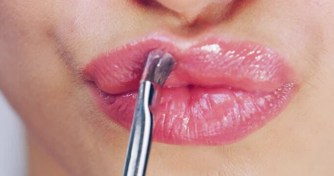 Creating the perfect pout. Close up of a woman pouting her lips while applying gloss with a lip brush. Woman applying pink lipstick to her lips