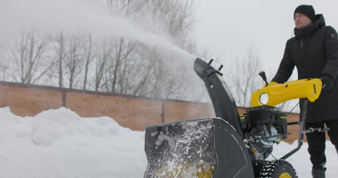 Man working with manual snow blower. Snowy winter. Man removes snow snowdrifts with Snowplough. Snowblower in action. Cold weather. Slow motion