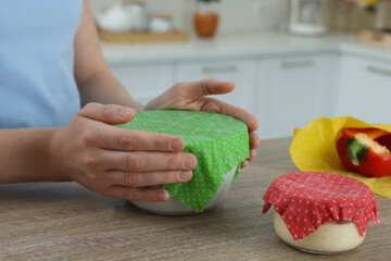 Woman holding bowl covered with beeswax food wrap at wooden table in kitchen, closeup
