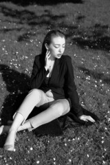 Black and white portrait of a young girl in the city park. Elegant and melancholy portrait, the girl is sitting on the grass. Beautiful woman in classic clothes