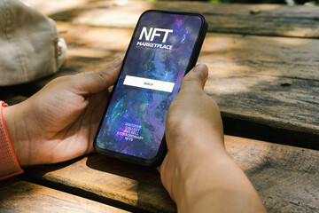 Girl in the park holding a smartphone with NFT (Non-Fungible Token) Marketplace app on the screen. Rustic wooden table