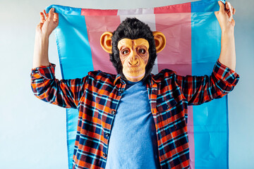 Man in monkey mask holding transgender flag.