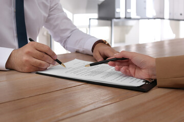 Businesspeople working with contract at wooden table indoors, closeup