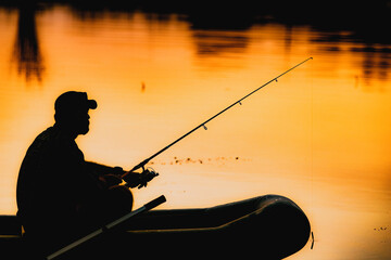 fisherman silhouette in a boat fishing on a lake at sunset