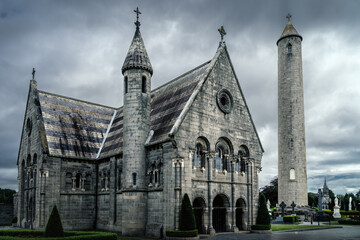 Beautiful, ancient mausoleum with Celtic cross and Round Tower in Glasnevin Cemetery, dramatic storm sky in background, Dublin, Ireland - obrazy, fototapety, plakaty
