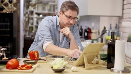 Man cooking in kitchen at home reading recipe on tablet. Healthy eating, diet, cooking application.