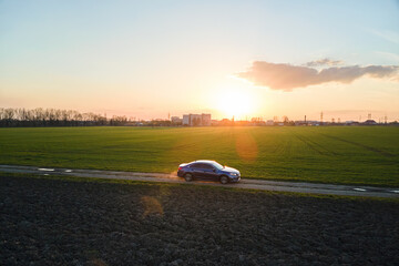 Aerial view of sedan car driving fast on dirt road at sunset. Traveling by vehicle concept