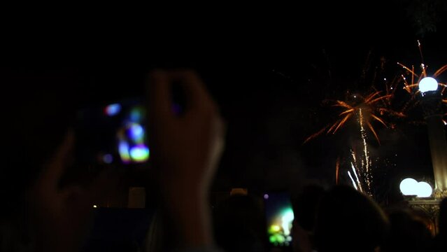 Crowd see fireworks and celebrating with photos by mobile telephone. Hand holding mobile smart phone, luxury bokeh light with firecracker background, crowd watching colorful fireworks