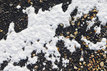 White snow spots on the dark gravel ground. Color abstract art photo for decoration or background.