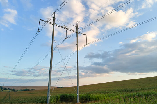 High voltage tower with electric power lines between green agricultural fields. Transfer of electricity concept