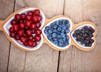 Portion wooden dish on light wooden background top view. Wooden partitioned dish divided into equal 3 section with berries