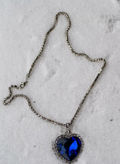 Close-up of the Heart of The Ocean necklace on snow. Titanic necklace. Blue diamond in a heart shape. Diamond necklace. - obrazy, fototapety, plakaty