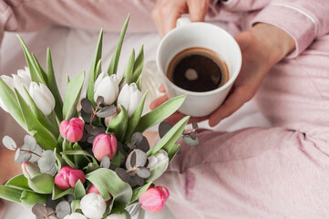 A bouquet of tulips and a cup of coffee in her hands.