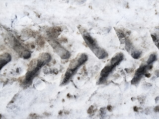Imprint of tractor or snowblower tire on road surface covered with dirty melting snow. Horizontal abstract winter road transportation background.