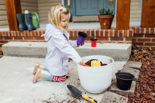 Little girl in rain boots digging in pot of dirt in Spring