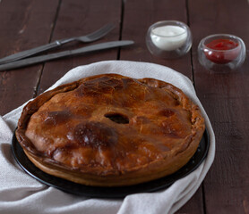English meat pie on a white napkin on a wooden brown table, next to a bowl of mayonnaise and ketchup