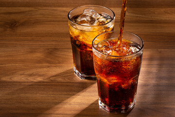 Coke glasses with ice cubes on wooden table.