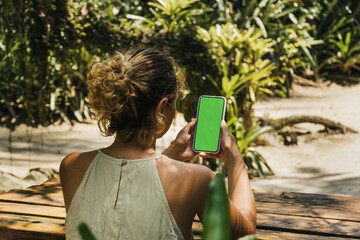 Girl in the park holding a smartphone with green screen app on the screen. Rustic wooden table....