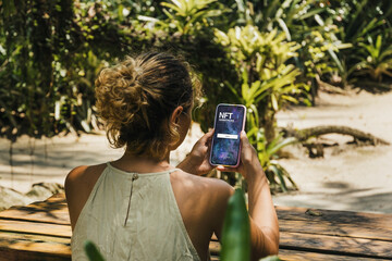 Girl in the park holding a smartphone with NFT (Non-Fungible Token) Marketplace app on the screen....
