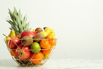 Metal bowl with different fresh fruits on white marble table. Space for text