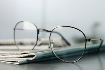 Stack of newspapers and glasses on grey table indoors, closeup