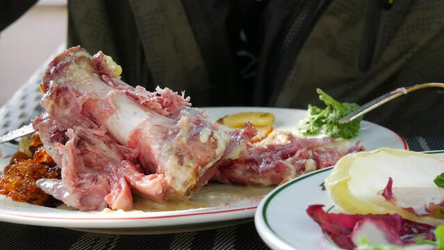 Male hands cut a pork knuckle with a fork and knife in a restaurant on the street