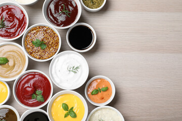 Many different sauces and herbs on wooden table, flat lay. Space for text