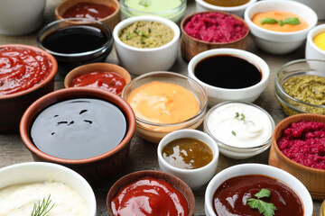 Many bowls with different sauces and herbs on wooden table