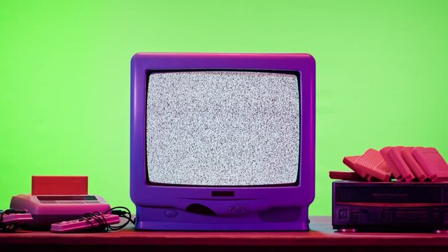 Old television with grey interference screen on purple neon background. Close-up of vintage tv and cartridges for retro playstation. Antique video game, nostalgia. 