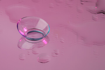 Contact lens on wet pink reflective surface. Space for text