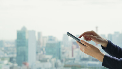 都市を背景にスマートフォンを使う女性