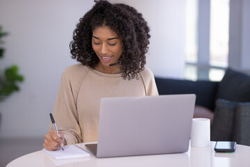 Young black woman at home remote working on laptop computer talking to her colleague
