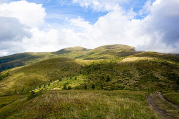 Green valley high on the mountains. View to blue sky with white clouds in summer day. Summer landscape