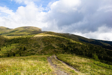 Country road in green mountains. Background with white clouds and blue sky on a warm sunny summer day