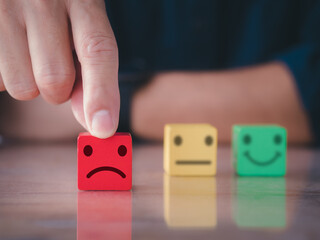 Customer satisfaction survey concept. Close up customer hand choose unhappy face, blurred neutral and smiley face icon on wood cube to survey feedback, rating, review, service satisfaction.