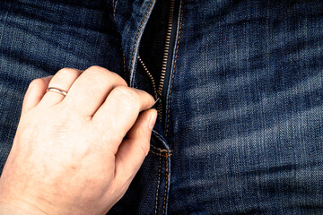 The zipper on the jeans is unfastened by hand.