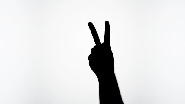 Man showing peace gesture with fingers isolated on white background. Male person making shadow silhouette with hand close-up.