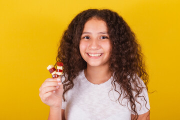 Afro-Brazilian, latin-american girl with curly hair smiling, holding cheese and guava skewers,...