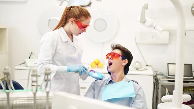 Young female dentist in UV protective glasses using dental curing light during composite filling