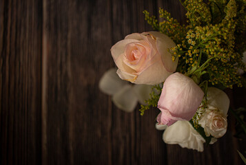beautiful romantic nostalgic background with bouquet of pastel color roses and small yellow flowers on dark wood floor