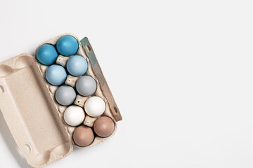 Easter eggs pastel colored in egg box on light background with copy space. Minimal Easter celebration concept, dyed chicken egg with color gradient from blue to beige coloured in carton pack